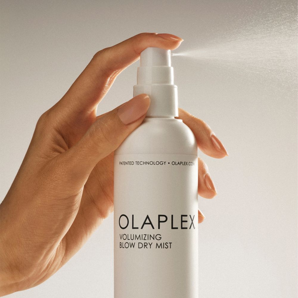 Hand sprüht Olaplex Volumizing Blow Dry Mist. Weiße Flasche, Sprühnebel sichtbar.