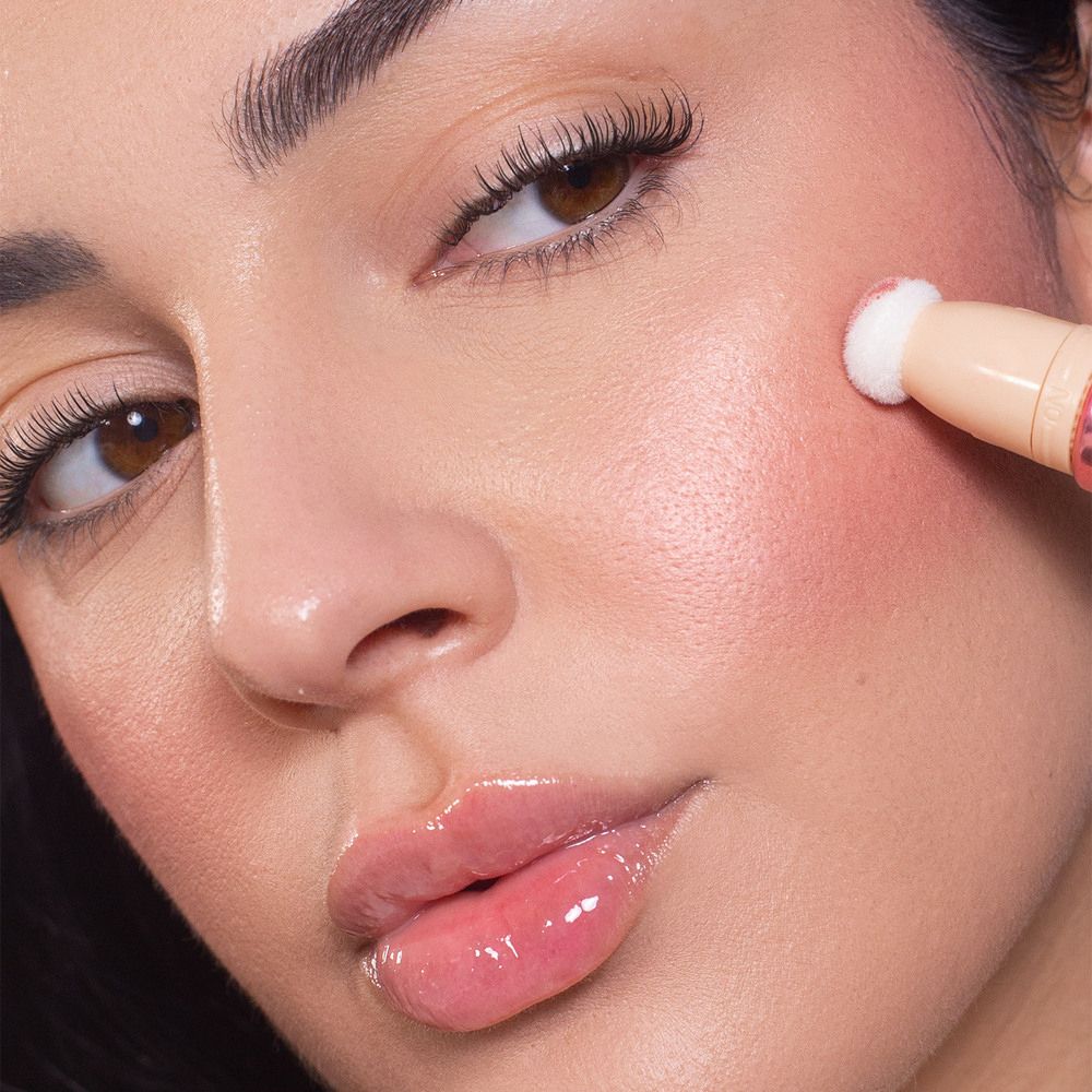 Viso di donna con blush. Applicatore sulla guancia. Pelle lucida. Sopracciglia definite. Labbra lucide.