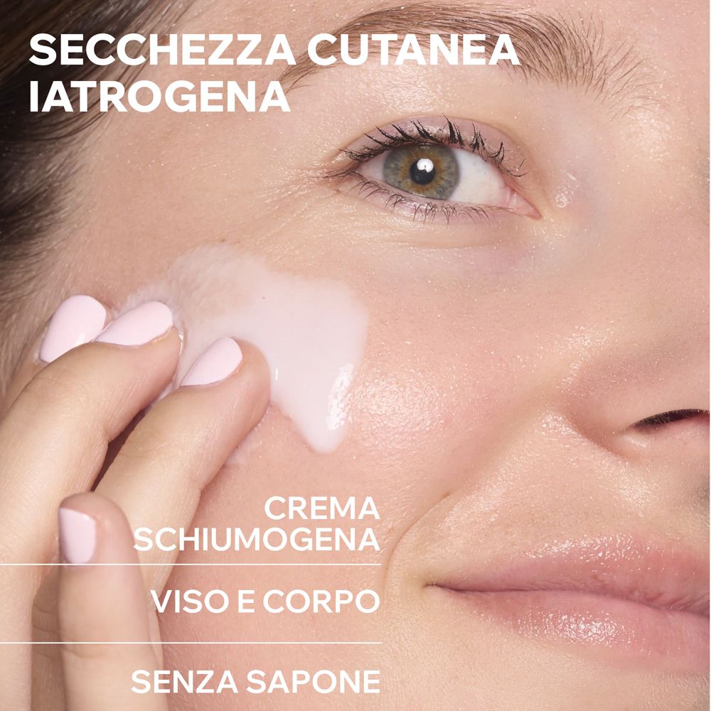 Nahaufnahme einer Hand, die eine schäumende Creme auf das Gesicht aufträgt. Text: SECCHEZZA CUTANEA IATROGENA, CREMA SCHIUMOGENA, VISO E CORPO, SENZA SAPONE.