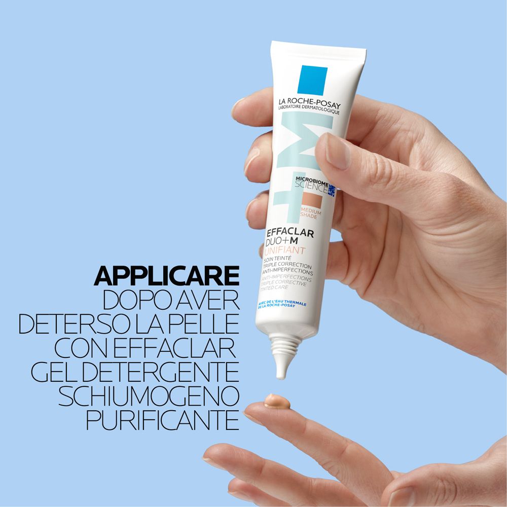 Hand hält Tube Effaclar Duo+M Unifiant. Produkt wird auf Finger aufgetragen. Hintergrund: blau.