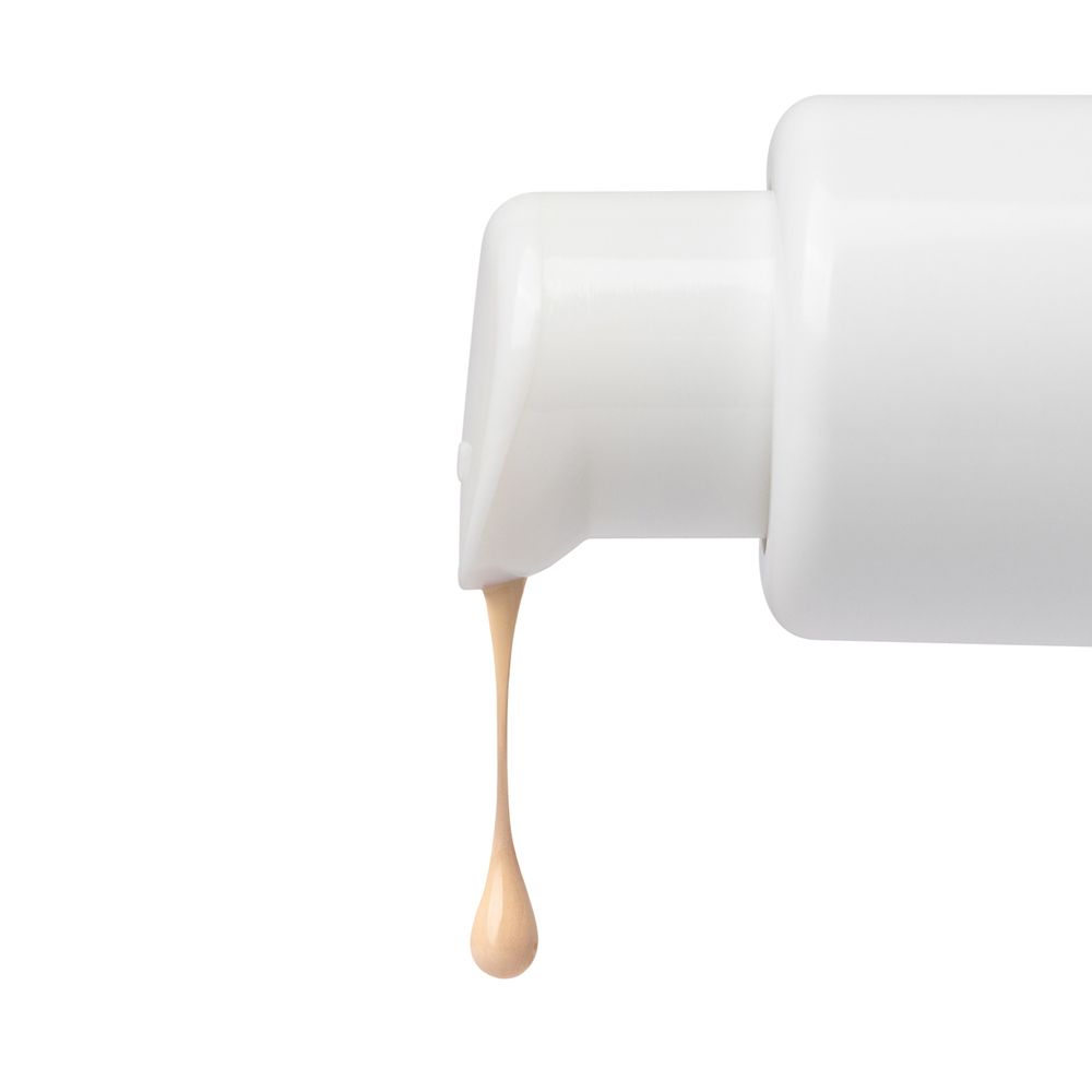 Primo piano di un fondotinta che gocciola da un flacone. Il liquido è beige.
