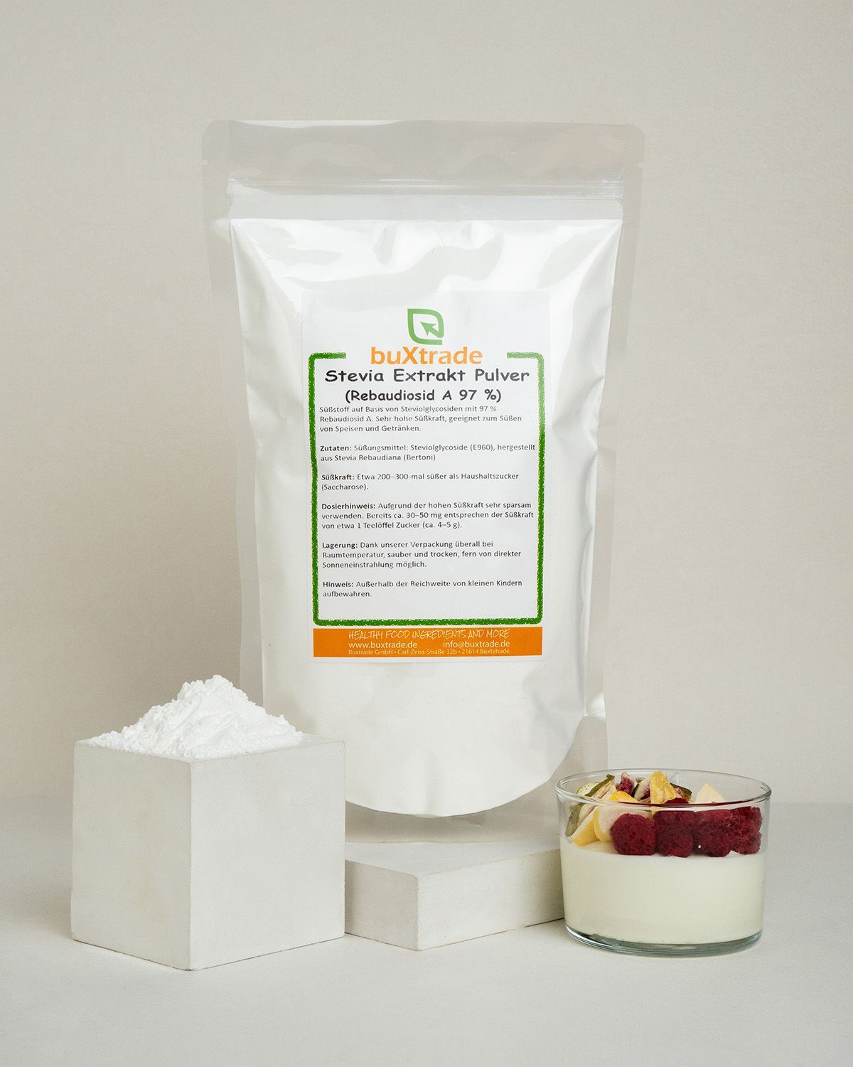 Stevia-Pulver in einem Würfel, daneben eine Verpackung und ein Glas mit Joghurt.
