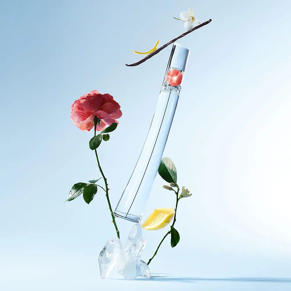 Eine transparente Flasche mit roter Blume, umgeben von Blumen, Zitrone, Vanille und Eis. Auf blauem Hintergrund.