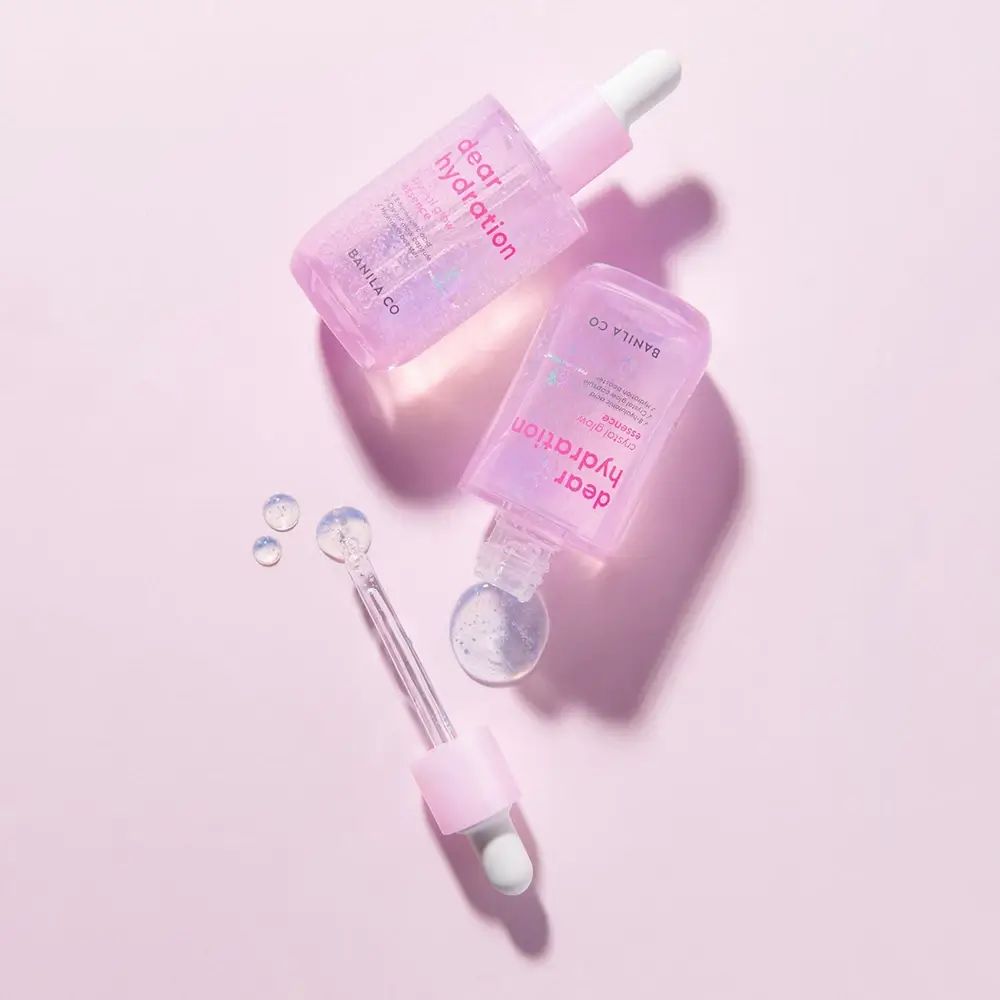 Zwei rosa Serumflaschen mit Pipetten. Aufschrift: dear hydration. Marke: BANILA CO. Hintergrund: rosa. Einige Tropfen Serum.