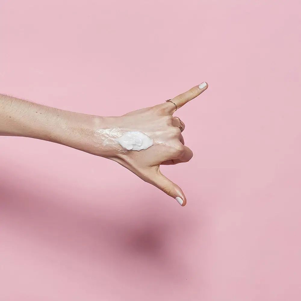 Hand mit Produkt auf dem Handrücken. Hintergrund: rosa.