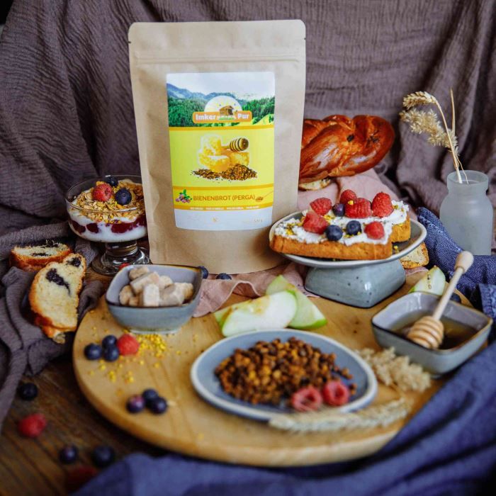 Produktpräsentation mit Bienenbrot (Perga) in einem Beutel. Auf einem Holzbrett angerichtete Speisen mit Honig und Obst.