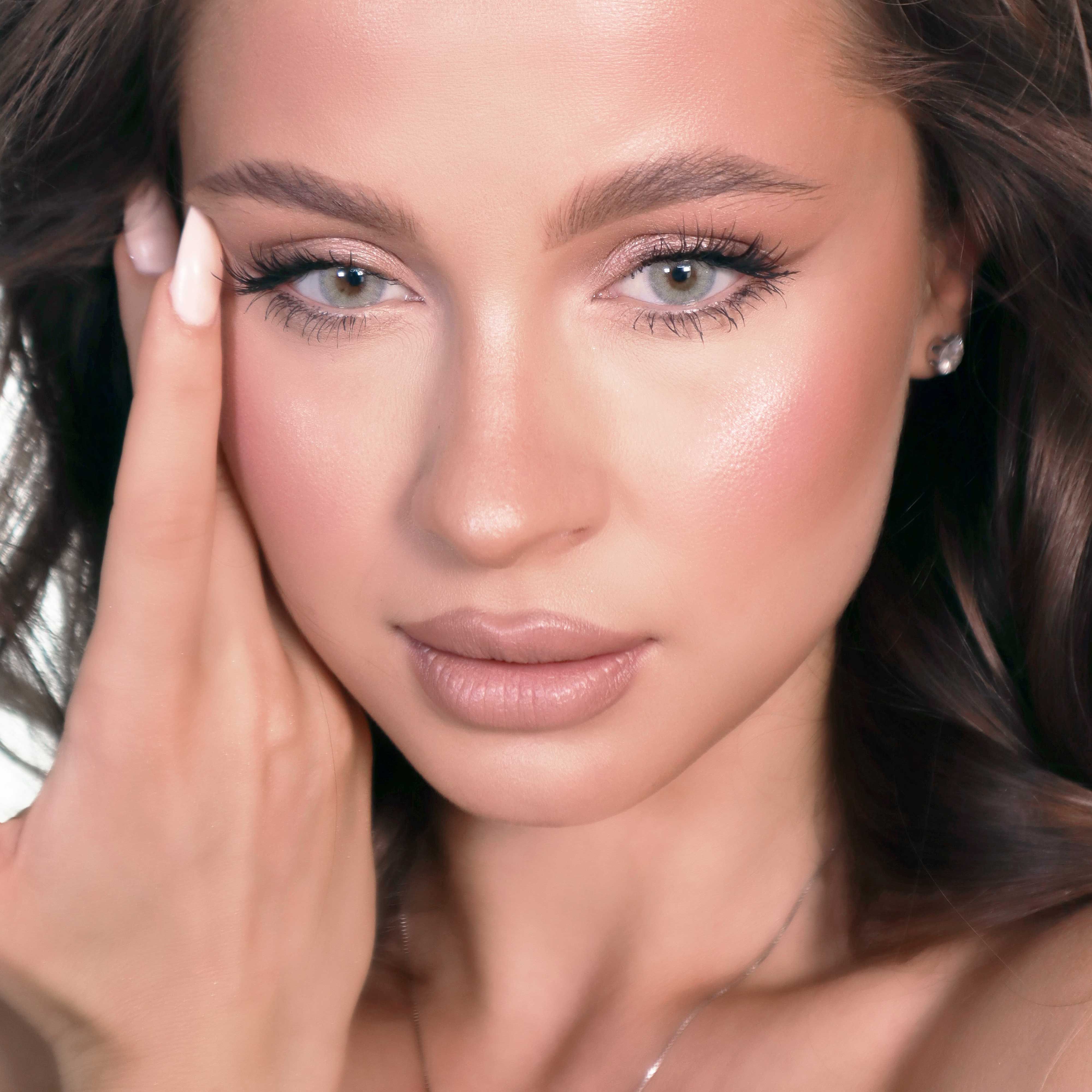 Porträt einer Frau mit grauer Kontaktlinse. Sie berührt ihr Gesicht mit der Hand. Deutliche Gesichtszüge.