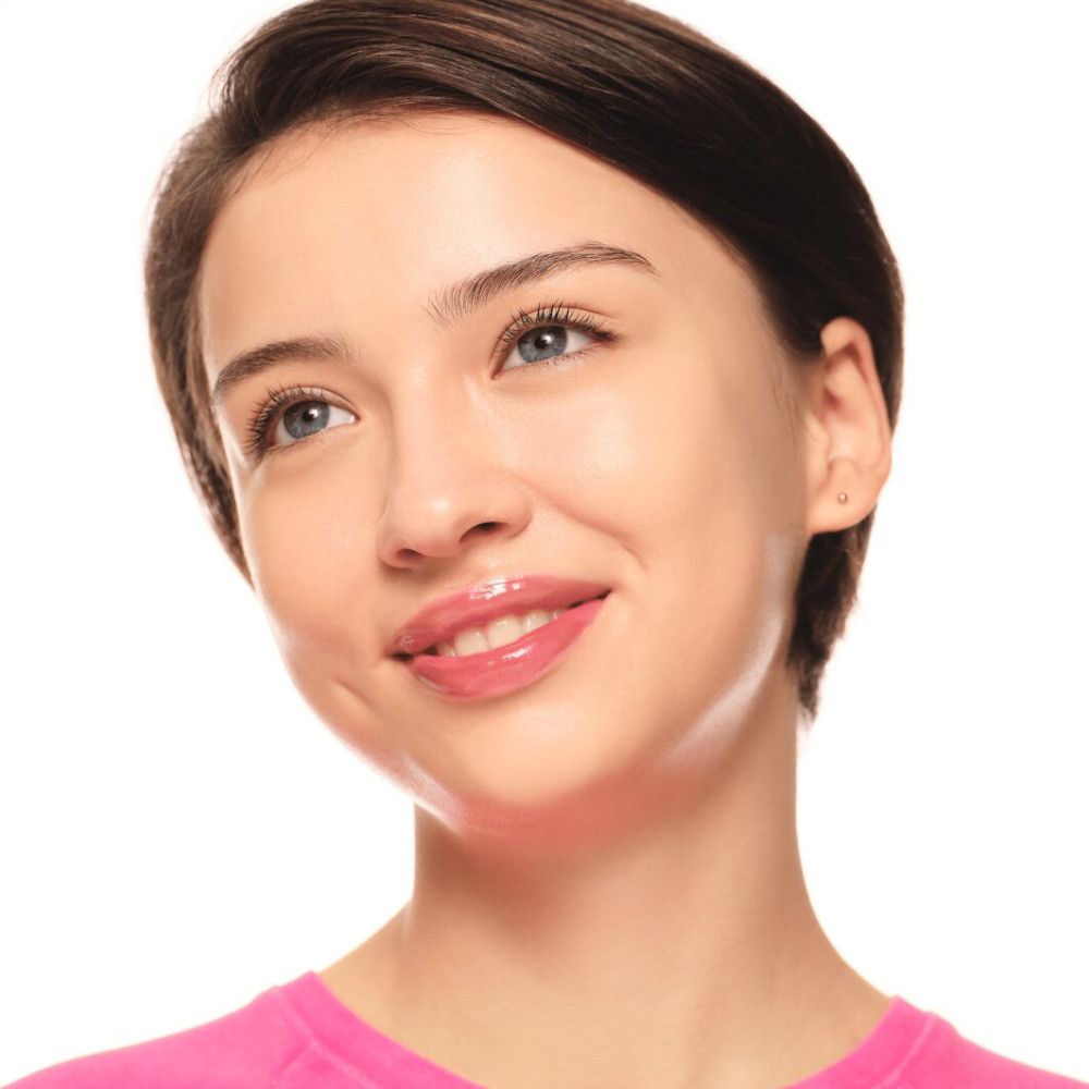 Porträt einer Frau mit glänzenden Lippen. Sie trägt ein rosa Oberteil.