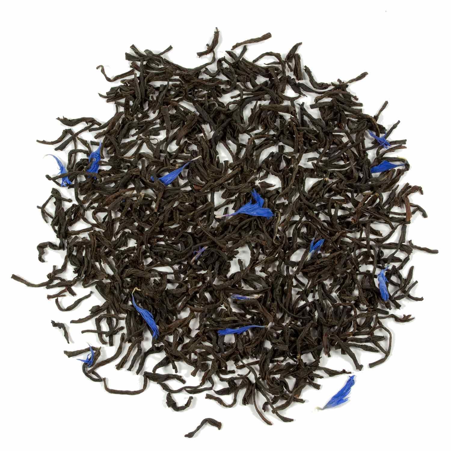 Lose Teeblätter mit blauen Blütenblättern. Dunkelbraune Blätter, kleine blaue Blütenblätter verstreut.