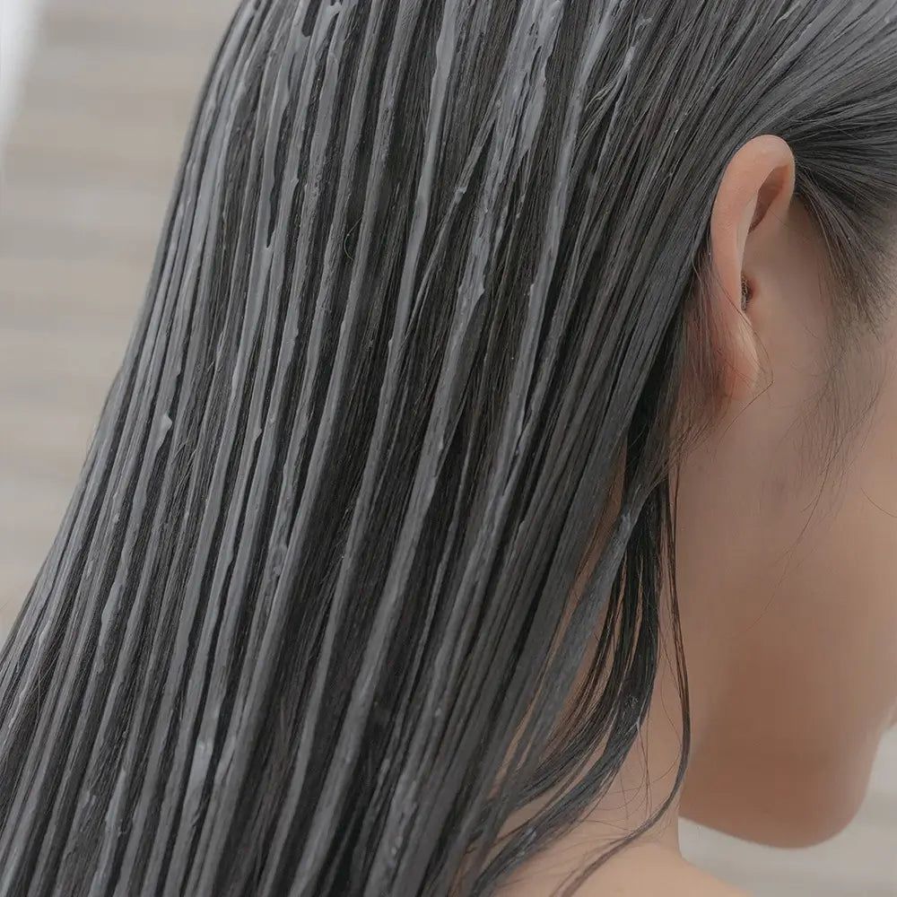 Nahaufnahme von Haar, das mit einer Creme bedeckt ist. Die Haare sind dunkel und nass.