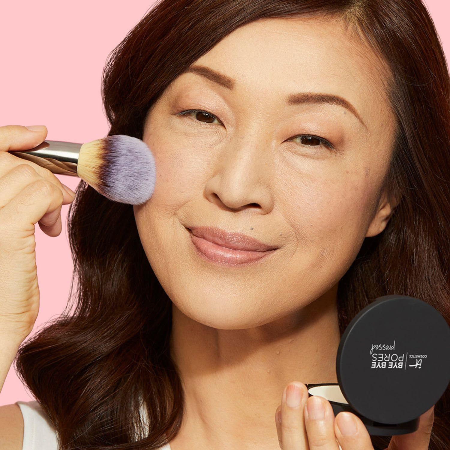 Frau trägt Puder mit Pinsel auf. Schwarze Puderdose mit Aufschrift: Bye Bye Pores pressed.