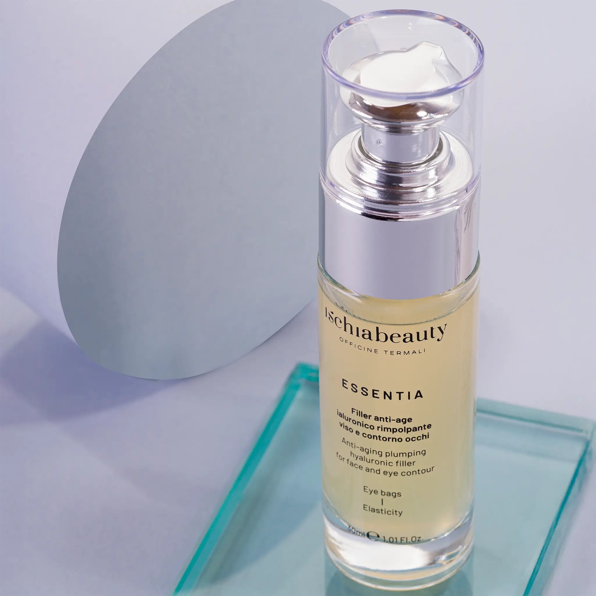 Glasflasche mit silberner Pumpe. Aufschrift: ischiabeauty, ESSENTIA, Filler anti-age, Augenringe, Elastizität. Auf Glasplatte.