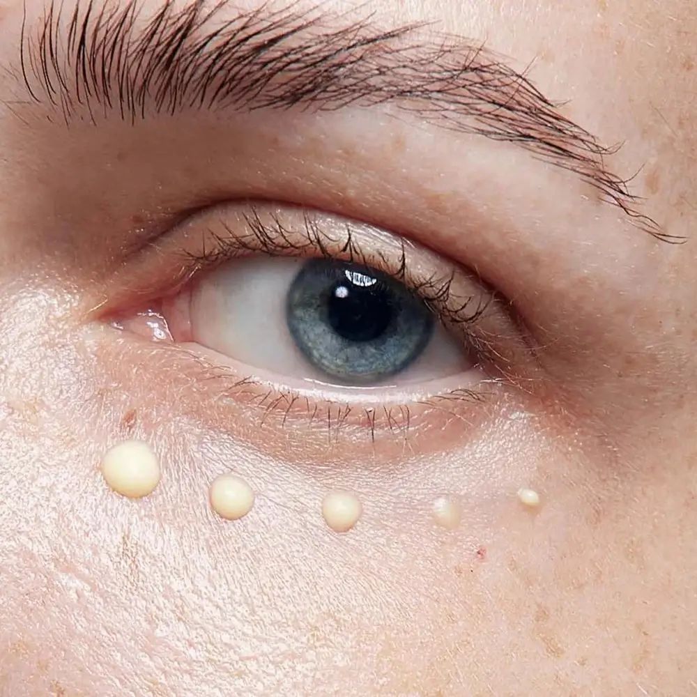 Nahaufnahme eines Auges mit Creme-Tropfen. Text: 'Peptides & Omegas Firming Eye Cream'.