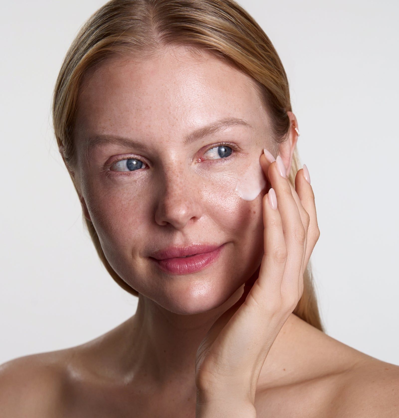 Frau trägt Serum auf die Haut auf. Helle Haut, blonde Haare, Blick nach rechts.