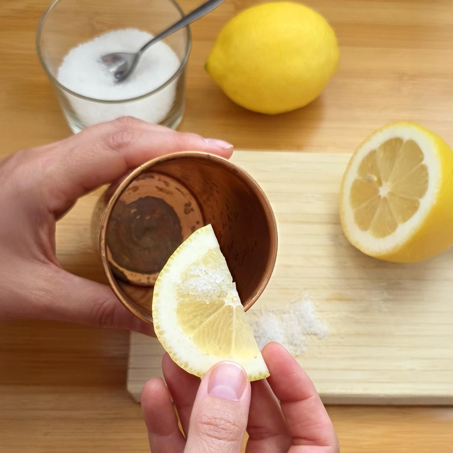 Hände mit Zitrone und Salz neben Kupferbecher. Holzbrett, Glas mit Salz.