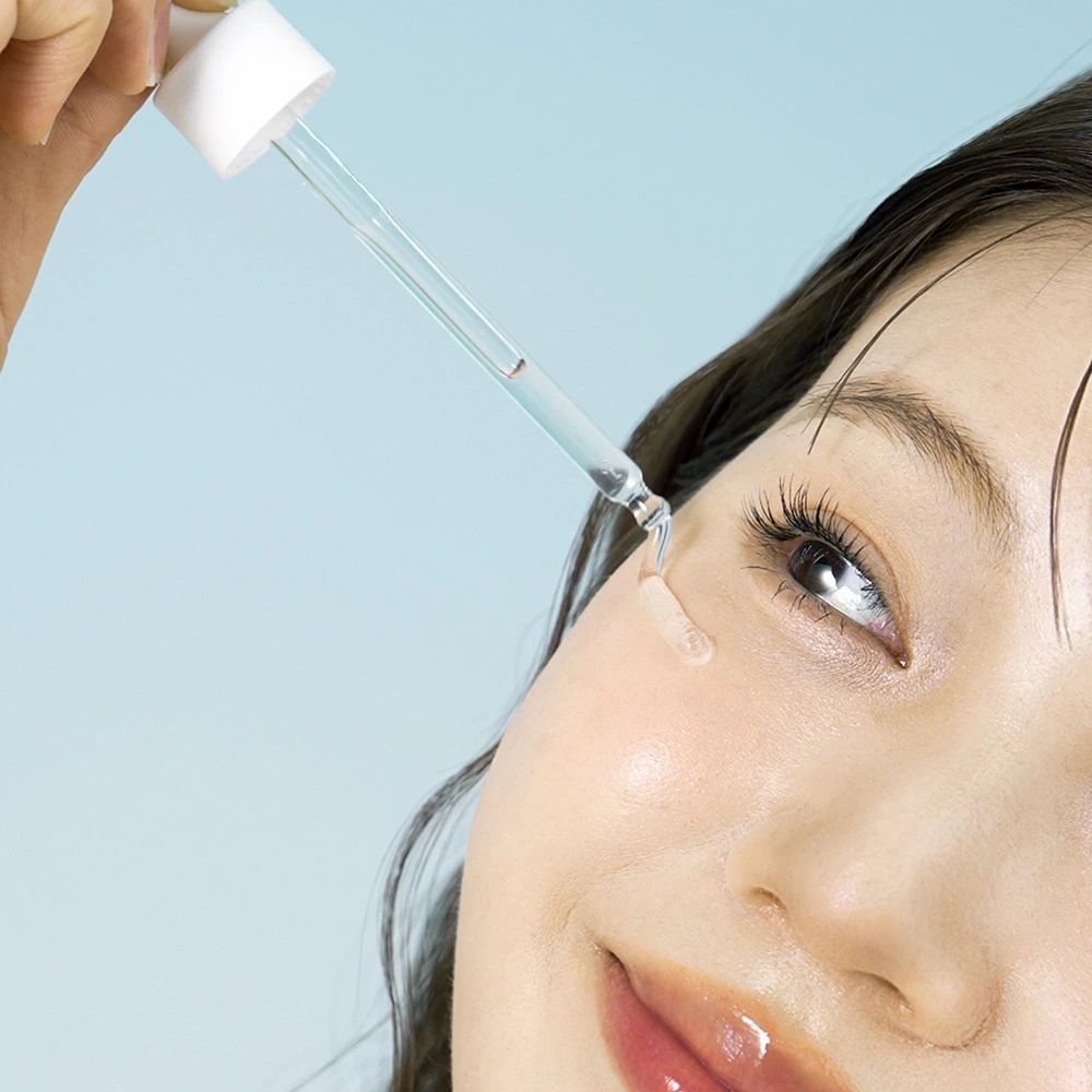 Nahaufnahme eines Gesichts, Serum wird mit Pipette aufgetragen. Helle Haut, blauer Hintergrund.