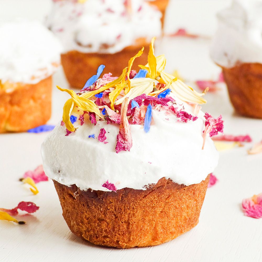 Cupcake mit weißer Creme und Blütenblättern. Mehrere Cupcakes auf weißem Untergrund. Blütenblätter verstreut.