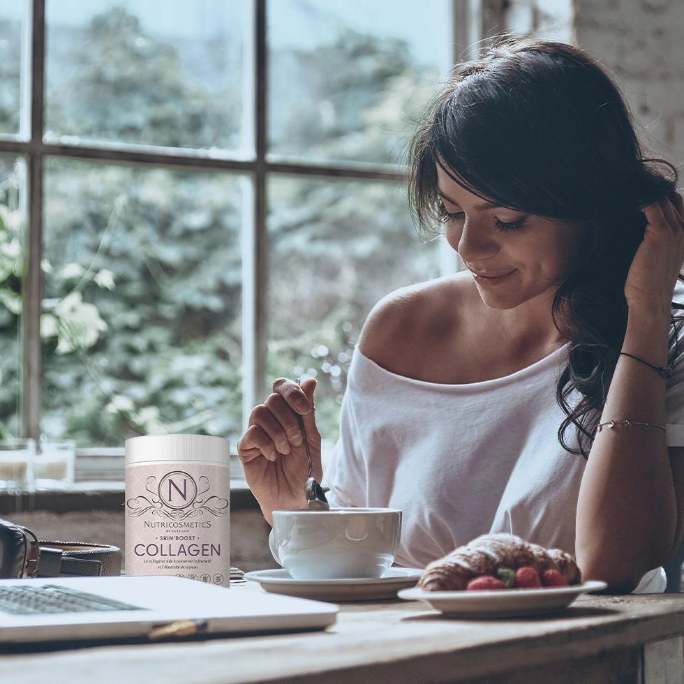 Frau am Tisch mit Kaffee und Kollagen-Pulver. Text: Nutricosmetics, Collagen. Auf dem Tisch: Laptop, Croissant, Erdbeeren.