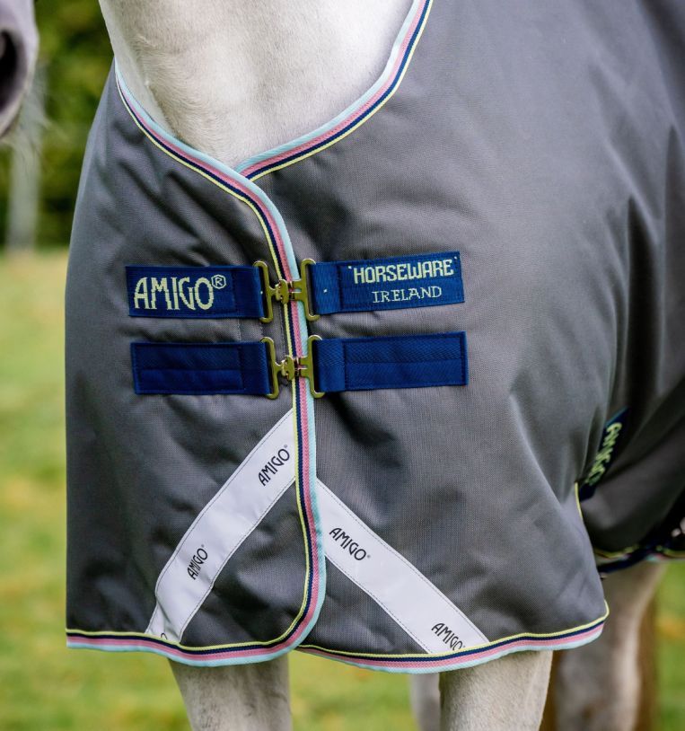 Nahaufnahme der grauen Pferdedecke. Blaue Verschlüsse mit der Aufschrift "AMIGO" und "HORSEWARE IRELAND".