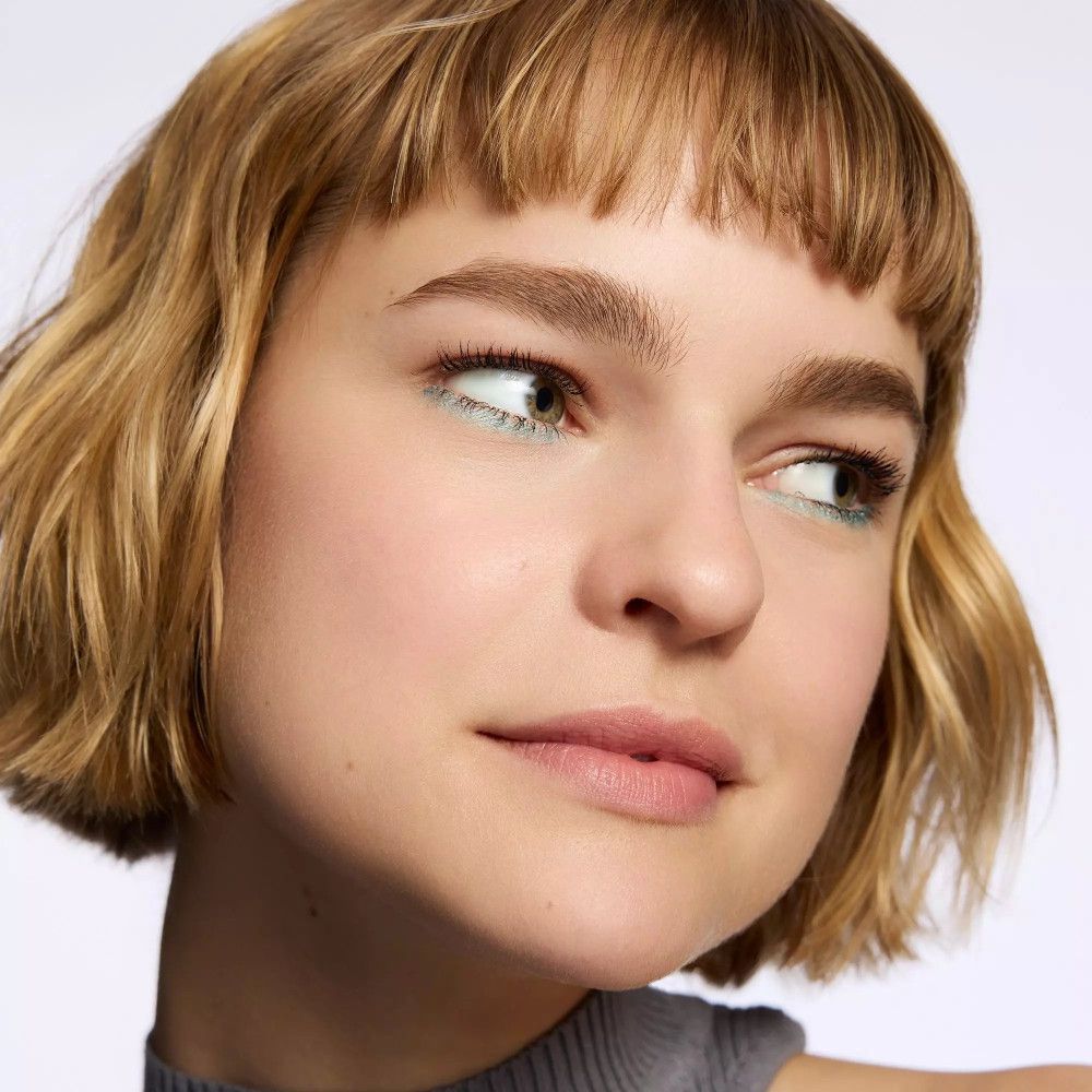 Nahaufnahme einer Frau mit hellblauer Lidschattenfarbe. Sie blickt zur Seite. Hautton ist hell.