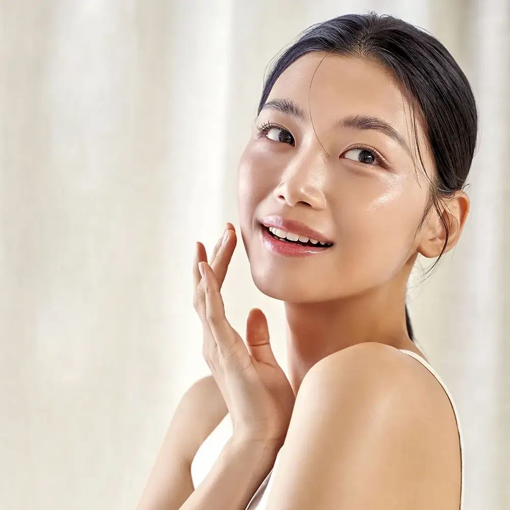 Frau berührt ihr Gesicht. Helle Haut, weißes Top. Hintergrund: hell.