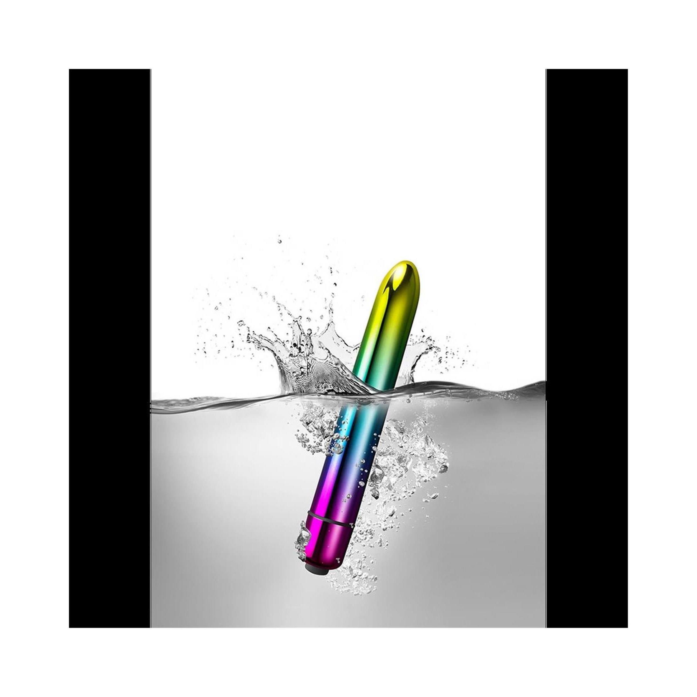 Zylindrischer Vibrator in Regenbogenfarben, der in Wasser eintaucht. Wasserspritzer sichtbar.