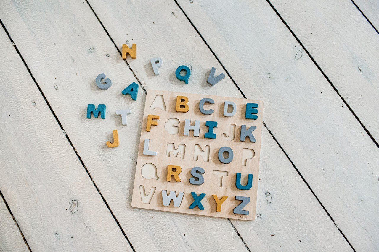 Holzpuzzle mit Buchstaben und Buchstaben daneben. Buchstaben in verschiedenen Farben. Das Puzzle ist quadratisch.