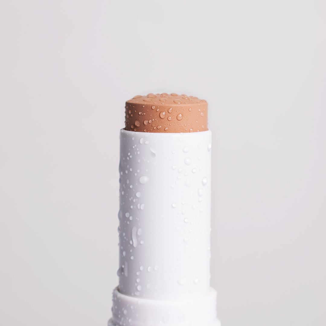 Nahaufnahme eines weißen Foundation Sticks mit beiger Spitze, bedeckt mit Wassertropfen.