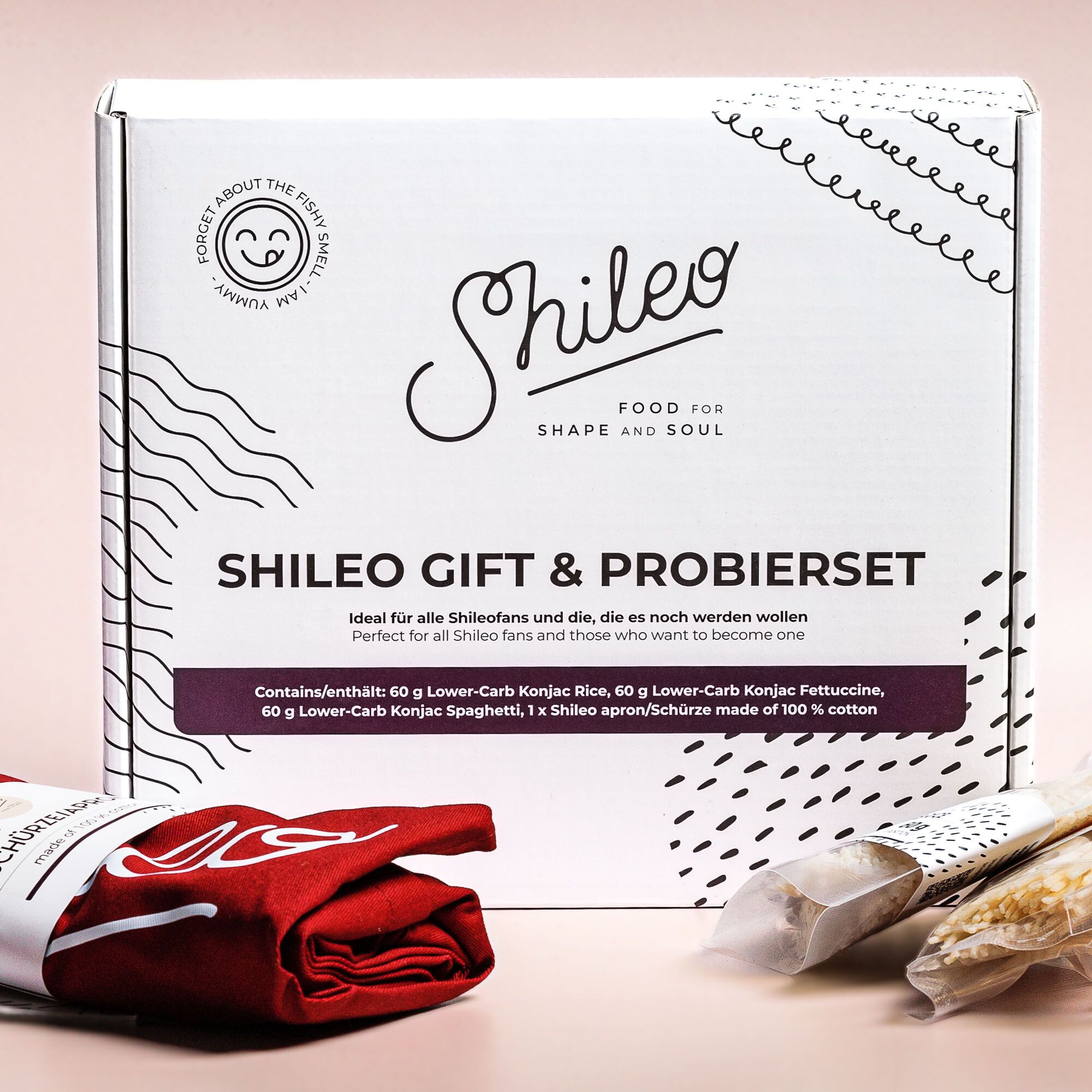 Geschenkset mit weißer Box, rotem Schürze und Konjak-Reis. Text: SHILEO GIFT & PROBIERSET.