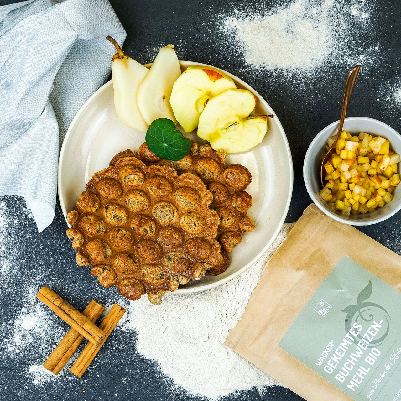 Teller mit Waffeln, Apfel- und Birnenscheiben. Daneben eine Schüssel mit Apfelwürfeln und ein Päckchen Mehl.