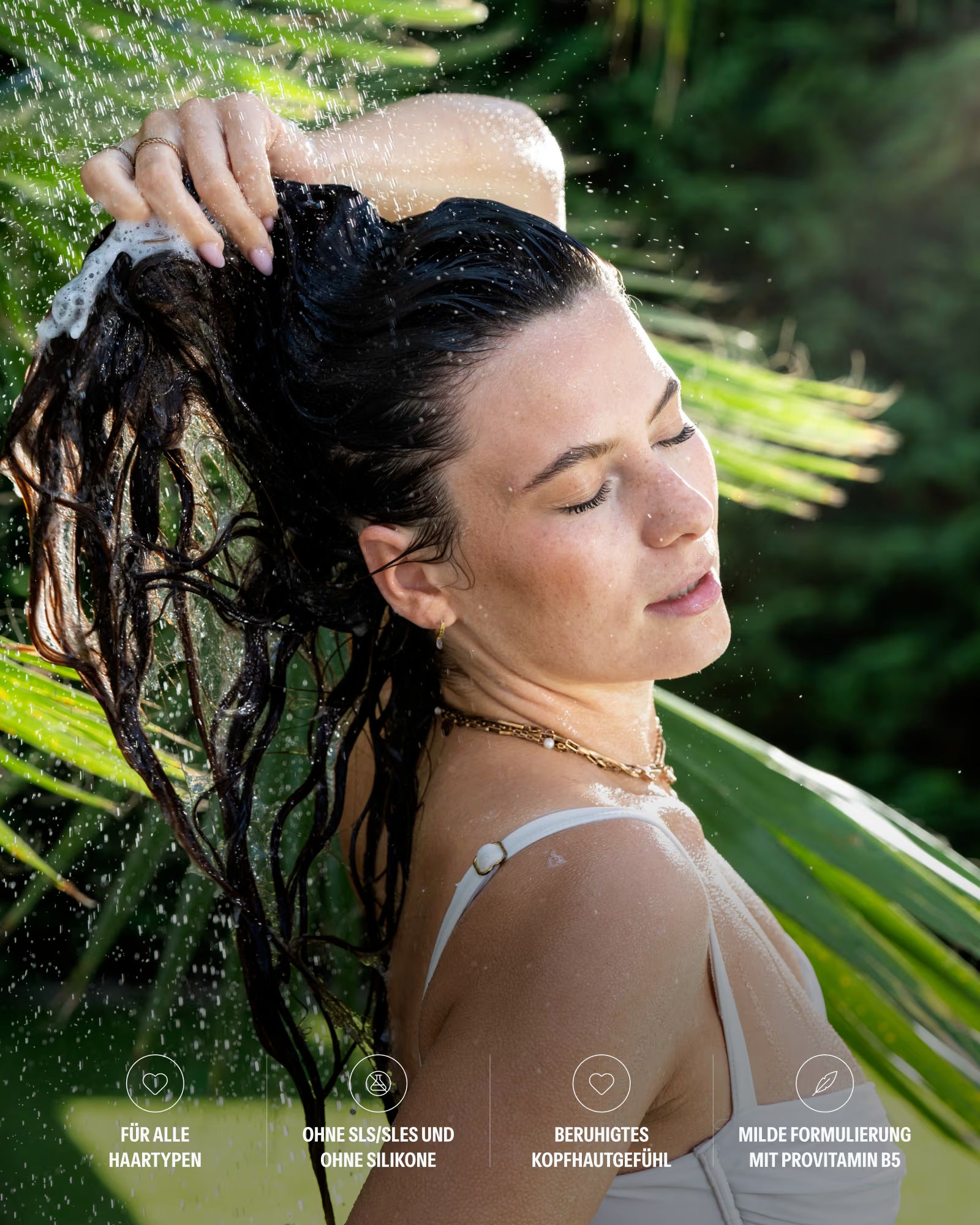 Frau wäscht sich unter der Dusche die Haare mit schäumendem Shampoo.