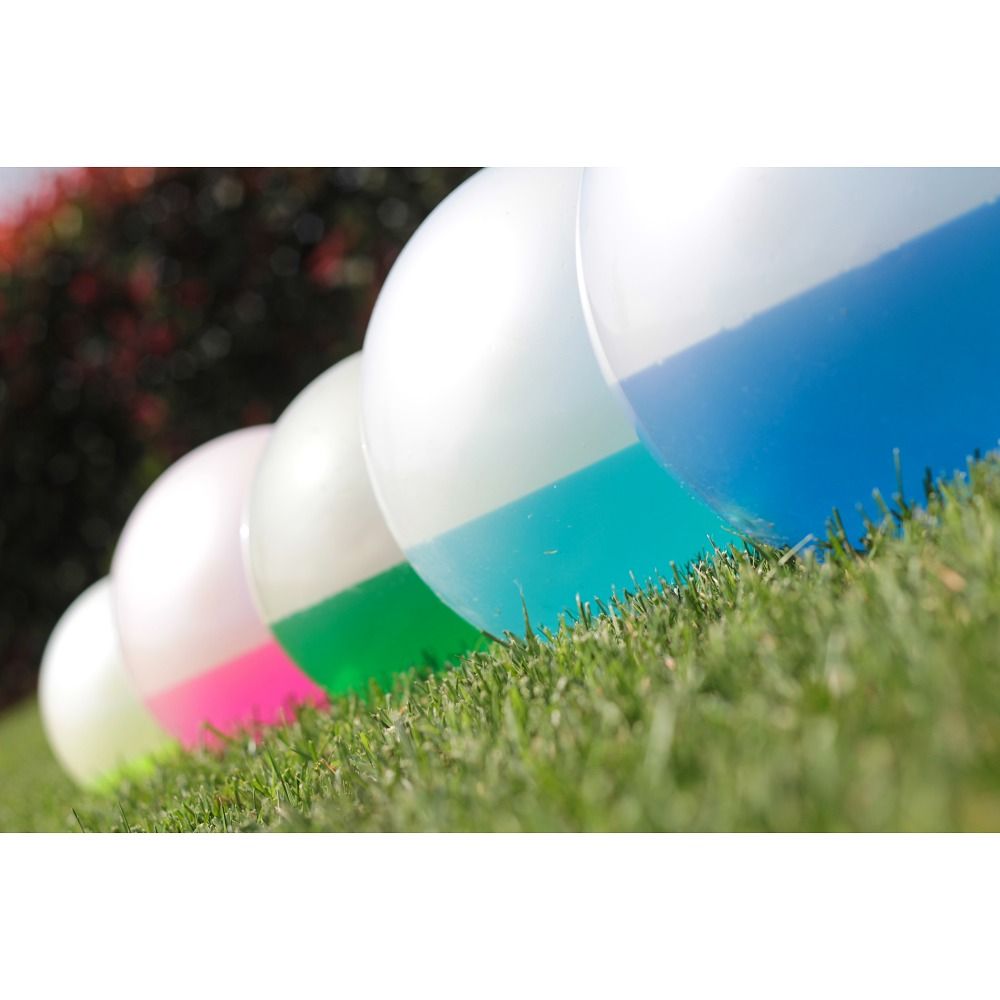 Reihe von Gewichtsballen auf Gras. Farben: weiß/pink, weiß/grün, weiß/blau. Teilweise im Gras.