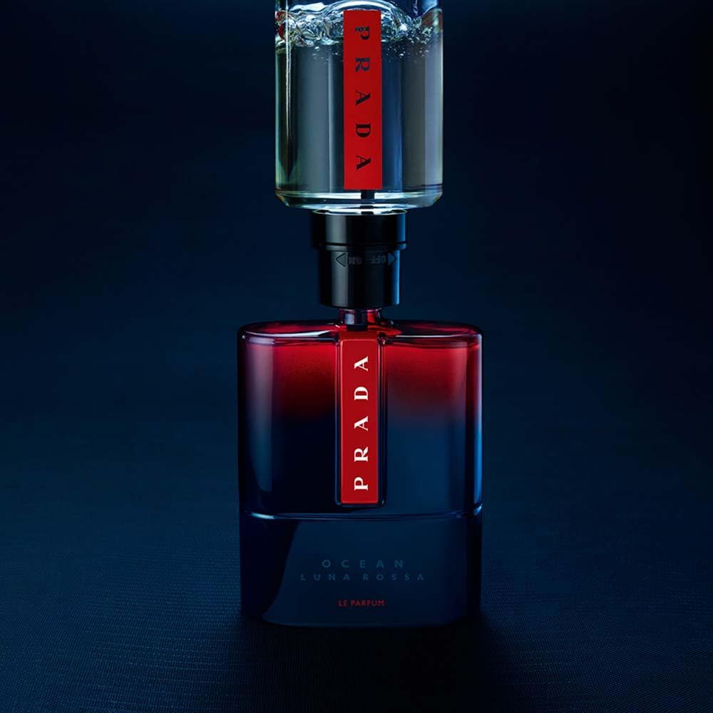 Flakon Prada Luna Rossa Ocean Le Parfum mit Refill-Flasche. Blaue Glasflasche mit rotem Prada-Logo. Auf dunklem Hintergrund.