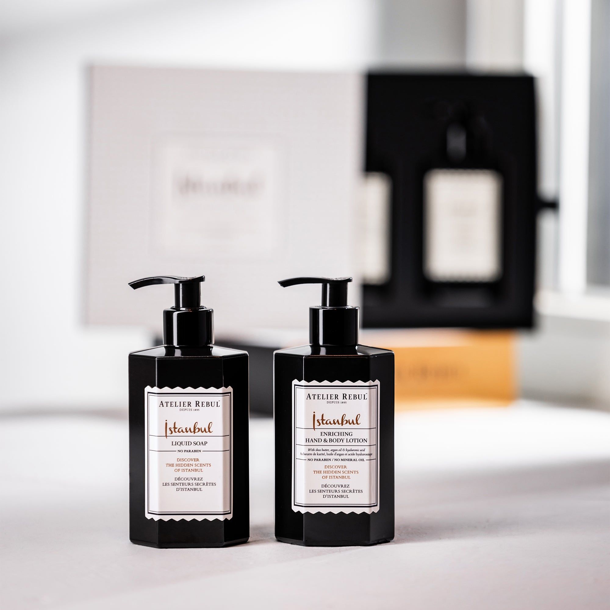 Zwei schwarze Seifenspender mit Etiketten. Im Hintergrund eine Geschenkbox und eine weitere Flasche. Aufschrift: Atelier Rebul Istanbul.