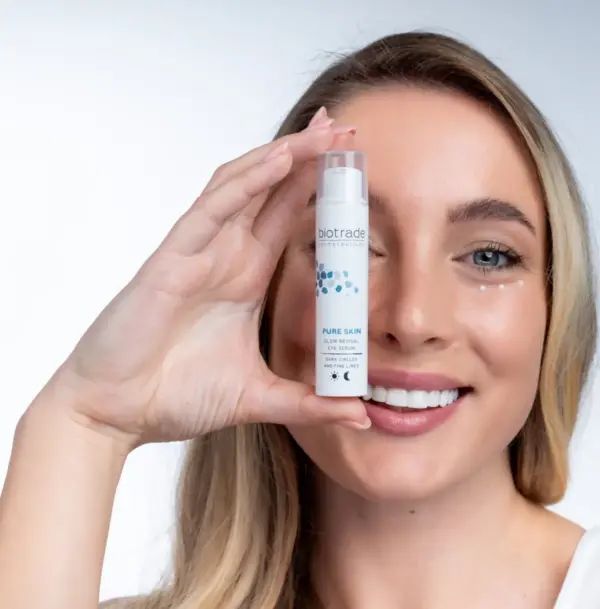 Frau hält weißen Zylinder, Biotrade-Logo, Pure Skin Glow Revival Eye Serum, gegen Schwellungen, Augenringe und feine Linien.