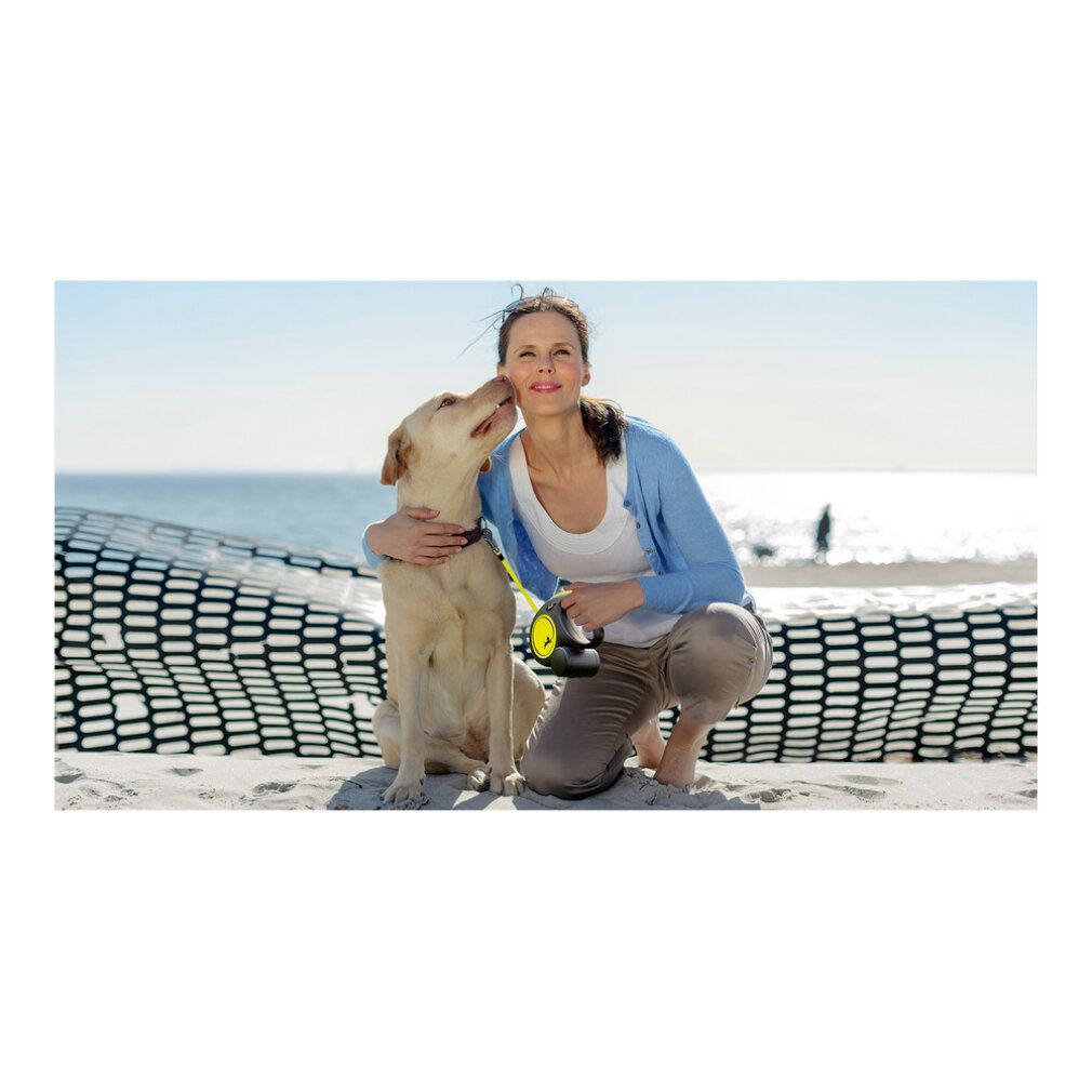 Frau mit Hund am Strand. Frau kniet, Hund sitzt. Gelbe Hundeleine. Meer und Himmel im Hintergrund.
