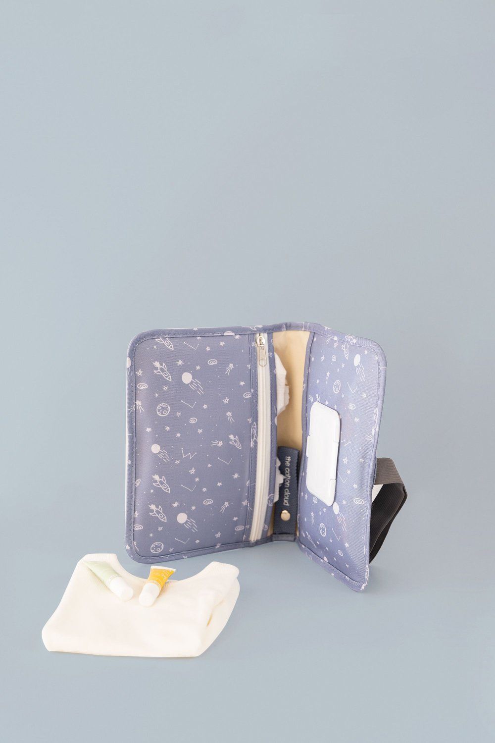 Geöffnete Windeltasche Cosmic mit Wickelunterlage, Cremes und Feuchttüchern auf blauem Hintergrund.