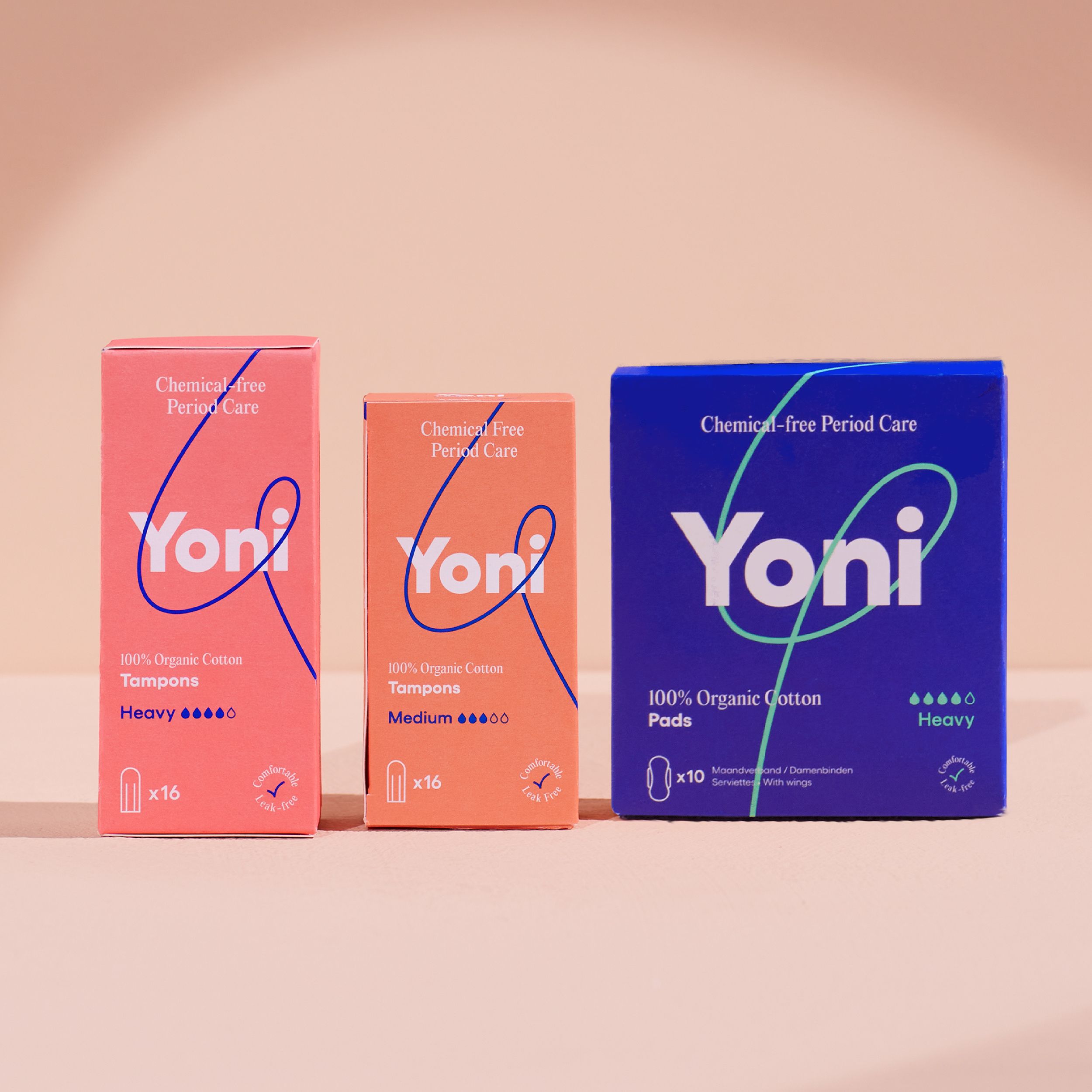Drei Schachteln mit Damenhygieneartikeln. Yoni-Logo. Pink, orange und blau. Aufdrucke: Tampons, Pads, Heavy, Medium.
