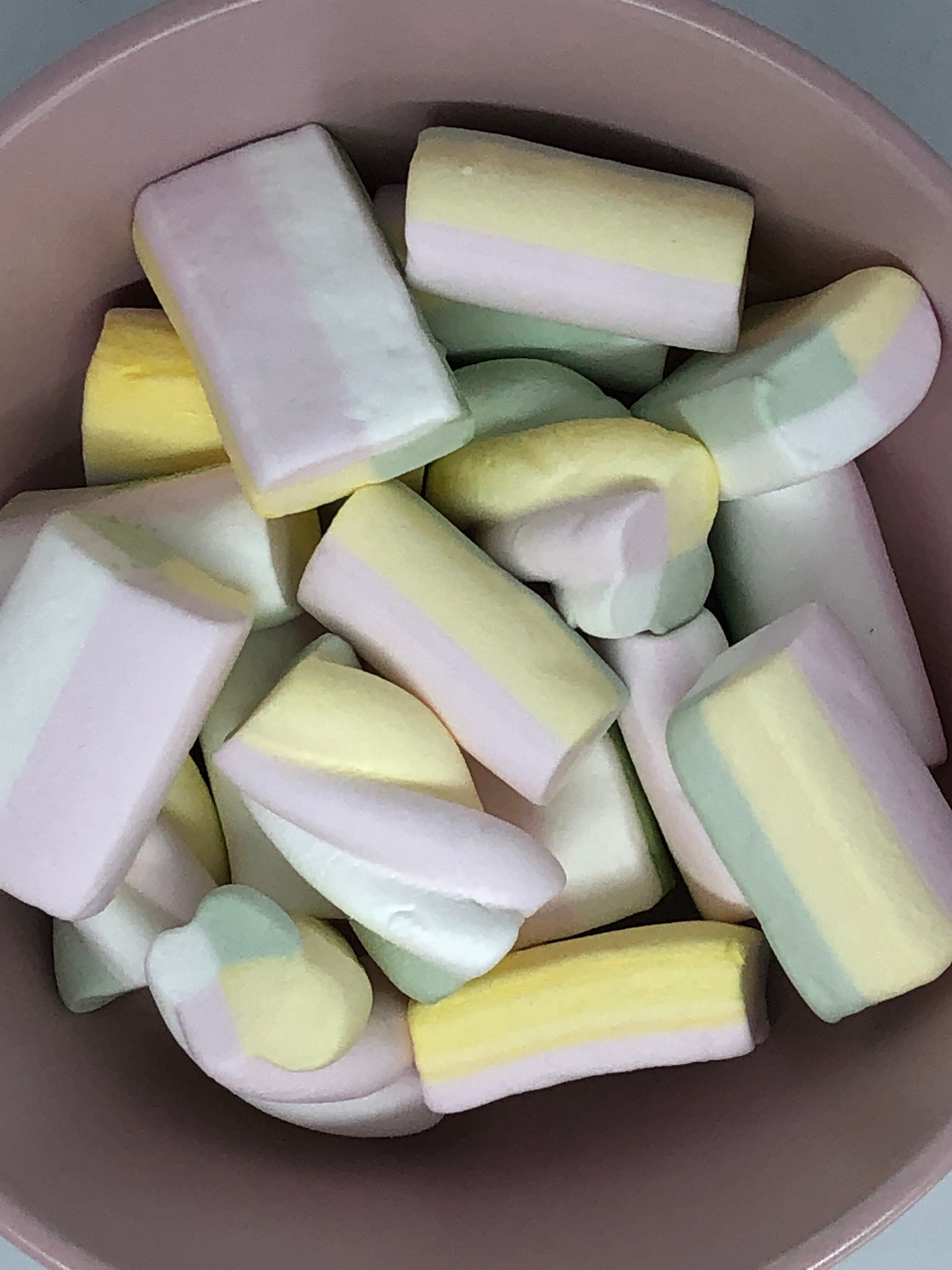 Rosa Schüssel mit farbigen Marshmallow-Twists. Gelb, rosa und grün gestreift. Nahaufnahme.