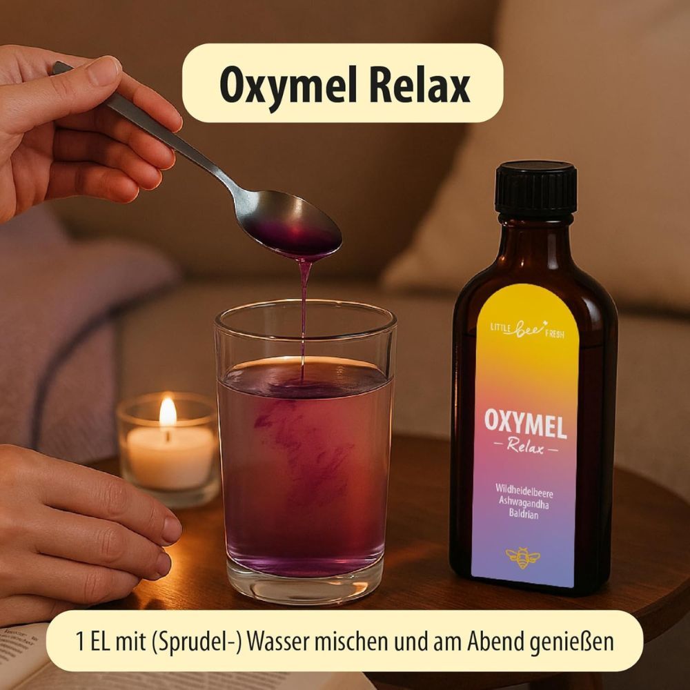 Glas mit Flüssigkeit, daneben Flasche mit Etikett "OXYMEL - Relax". Löffel mit Flüssigkeit. Kerze und Buch.