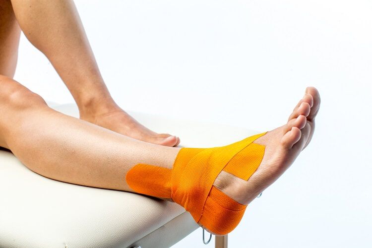 Orangefarbenes Kinesiotape am Fuß und Knöchel einer Person angebracht.
