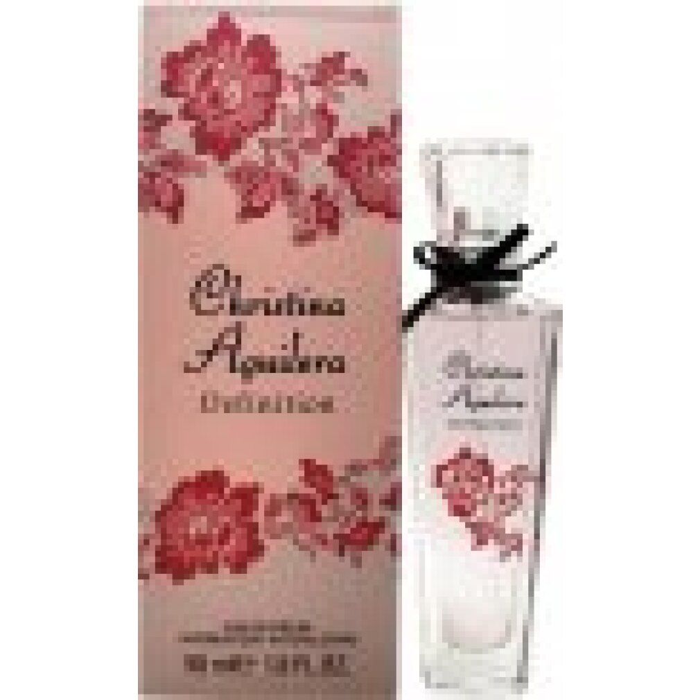 Parfümflasche neben Verpackung. Flasche: rosa Flüssigkeit, schwarze Schleife. Verpackung: Christina Aguilera Definition, floral.