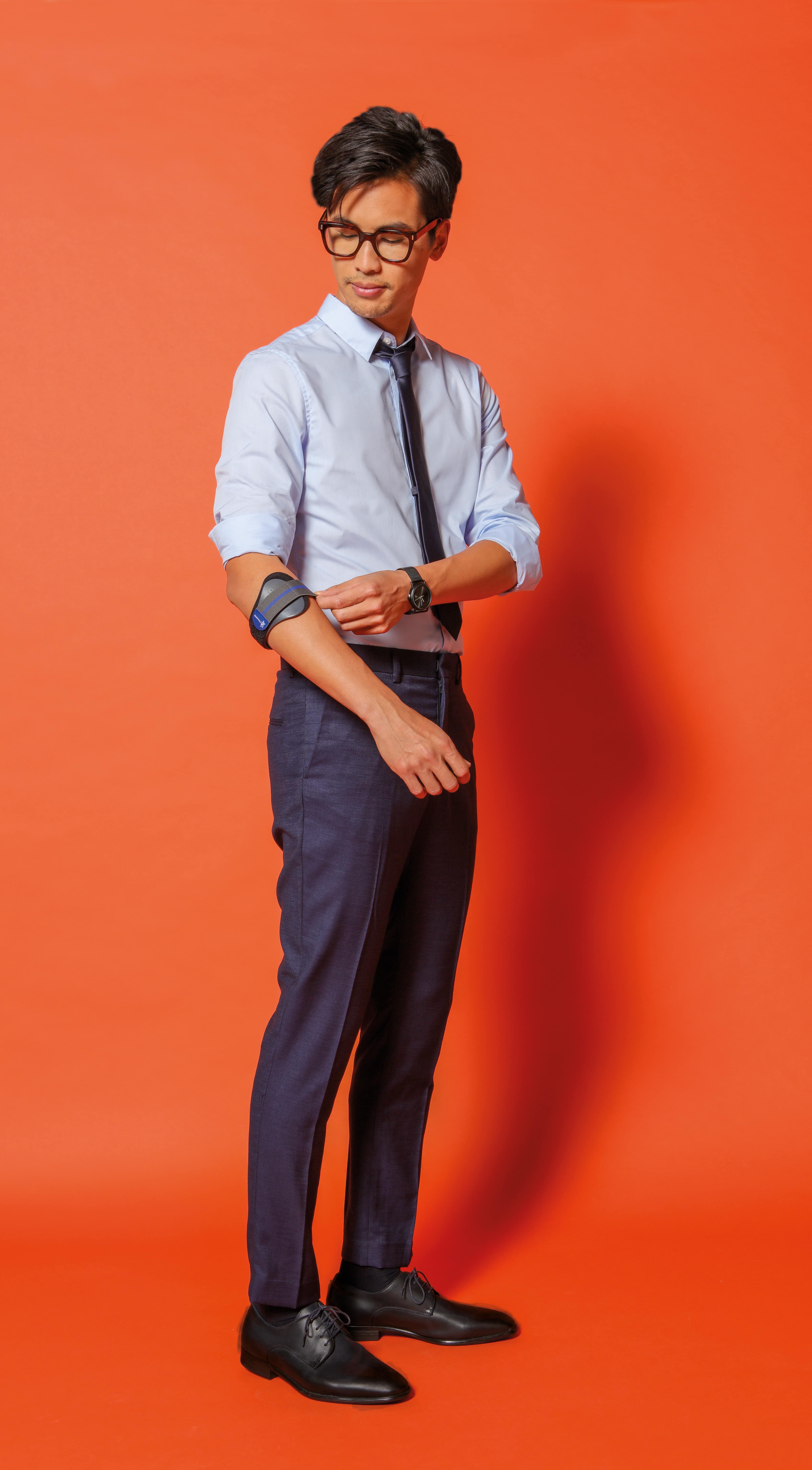 Mann mit Brille und Hemd, trägt eine Ellenbogenbandage. Orangefarbener Hintergrund.