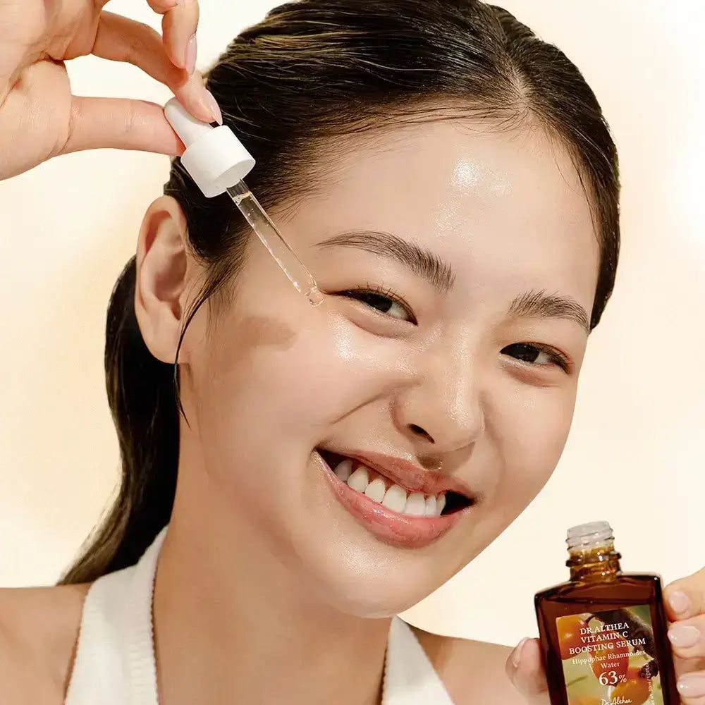 Frau trägt Serum mit Pipette auf. Serumflasche im Hintergrund. Frau lächelt.