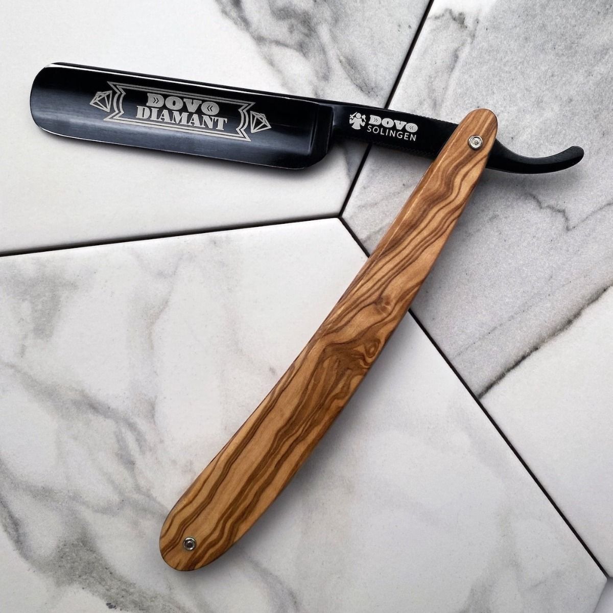Rasiermesser mit Holzgriff. Klinge mit Gravur "DOVO DIAMANT". Schwarze Klinge, Holzgriff. Auf Fliesenoberfläche.