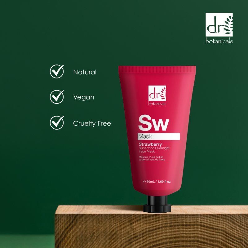 Rote Tube Dr. Botanicals Erdbeer-Gesichtsmaske neben Holzblock, mit Häkchen für 'Natürlich', 'Vegan' und 'Tierversuchsfrei'.