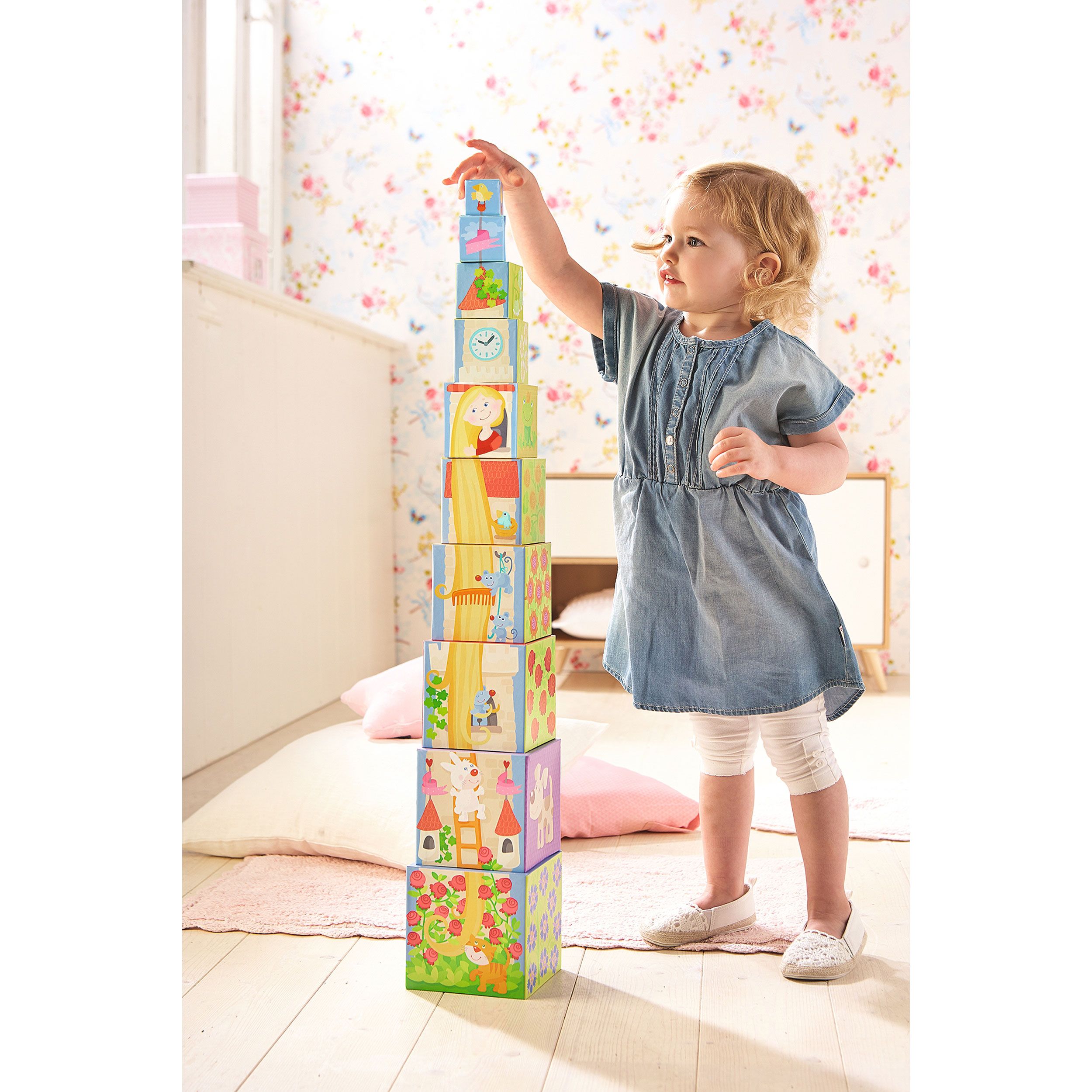 Kleinkind baut Turm aus Stapelwürfeln. Würfel mit Illustrationen von Rapunzel und anderen Motiven.