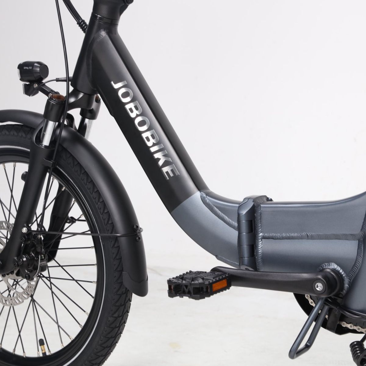 Detailansicht des E-Bikes. JOBOBIKE-Logo auf dem Rahmen. Schwarze Pedale und grauer Rahmen.