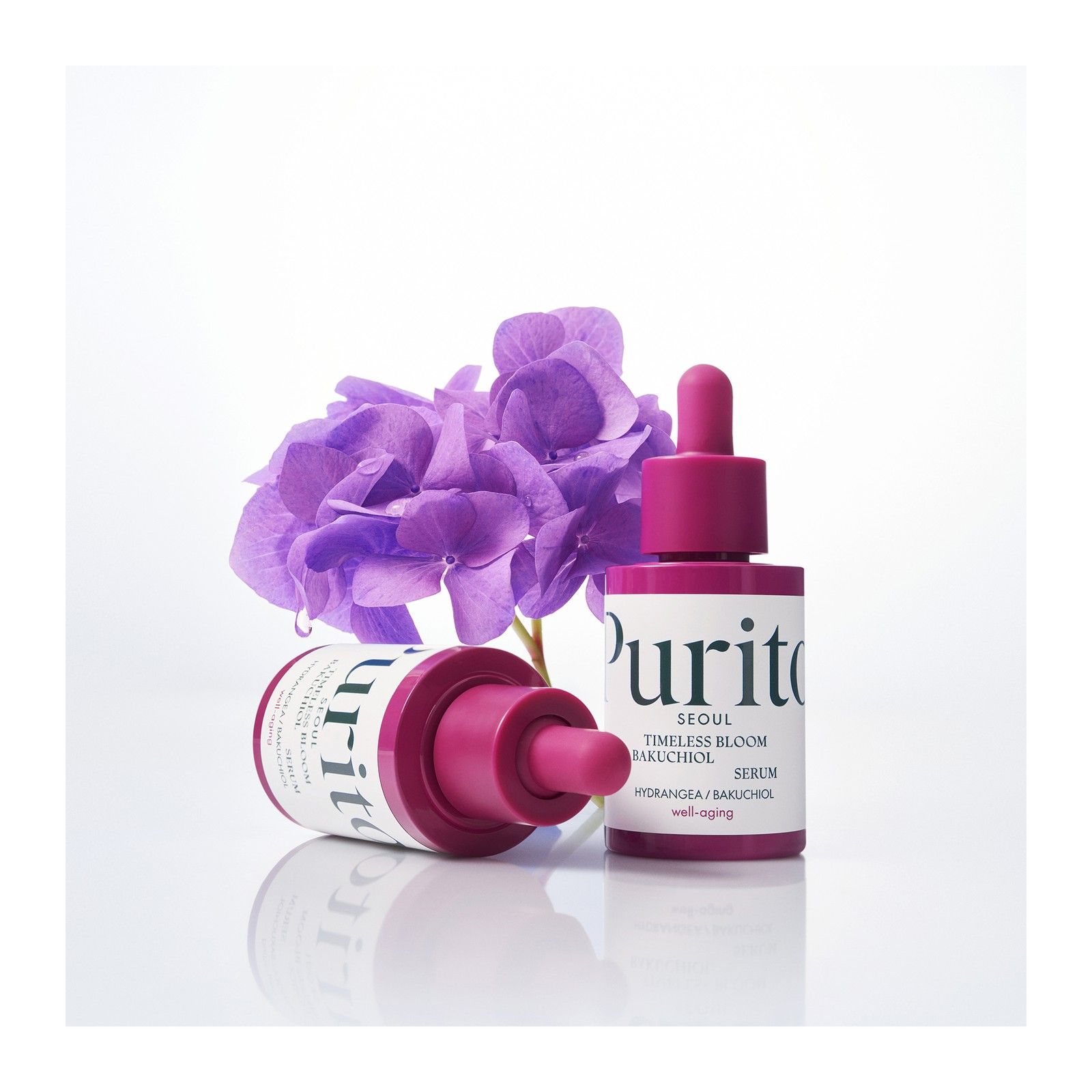 Zwei Flaschen Purito Bakuchiol Serum neben einer lila Hortensienblüte.