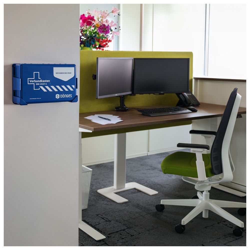 Blauer Verbandkasten an weißer Wand. Aufschrift: Verbandkasten DIN 13157-C, Logo und Schriftzug. Hersteller: dönges.